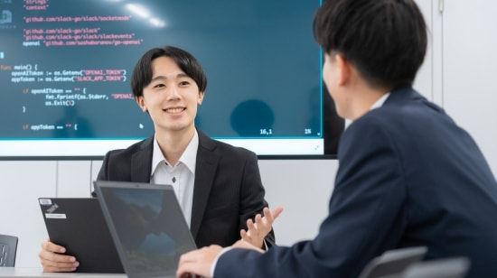 写真　パソコンの前で打ち合わせをするスーツの男女